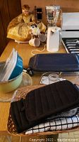 Kitchen items on a table including Osterizer blender, Pyrex casserole dish, black oven mitts, and various plastic containers