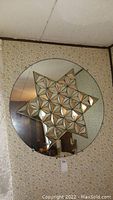 Large circular wall mirror with a three-dimensional star-shaped geometric frame composed of small triangular mirror segments, hanging on a wall with floral wallpaper.