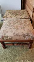 Image showing two floral upholstered ottomans placed side-by-side with wooden legs, one leg unscrewed on one ottoman, fabric shows rips and wear.