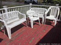 Full view of two plastic patio benches and two plastic chairs on red wooden deck, showing weathering and dirt spots.