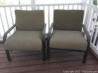 Front view of two weathered patio chairs with brownish-beige cushions on a wooden deck.
