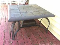 Full view of square metal patio coffee table with fire pit on a wooden deck.