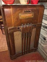 Front view of large Philco wood cabinet radio showing tuning dial, wood surface with wear, decorative grille, and controls.