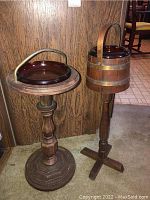 Two standing ashtray stands side by side showing overall structure and design, one wooden and one plastic/metal barrel style.