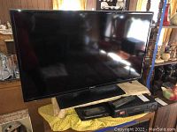 Samsung 40 inch flat screen TV on a low table with yellow towel and black VCR and DVD player stacked underneath.