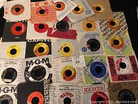Photo showing 25 assorted 45 RPM records in various colored labels and sleeves from different brands and labels.