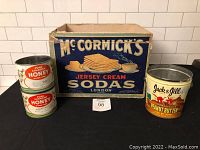 Photo showing the full set of four vintage product containers: two Pure Canada Honey tins stacked, one McCormick's Jersey Cream Soda cracker box behind them, and one Jack & Jill Peanut Butter tin to the right.