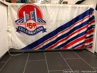 The full flag displayed horizontally on the floor showing the left side attached with a rope and the overall striped design on the right side.