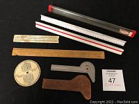 Top view of six measuring tools showing various rulers and scales including white architect scales, wooden ruler, metal slide rule, circular chart and wood-metal gauges.