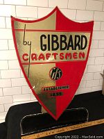Front view of the shield-shaped Gibbard Furniture advertising sign showing red and gold metallic colors with black and red text.