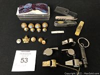 Full lot of buttons, pins, knives, whistles, and bow tie arranged on black surface, showing quantity and assortment of items.