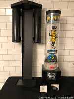 Full view of Planters vending machine with mounting bracket, clear cylindrical container featuring Mr. Peanut and product information, black base with coin mechanism.