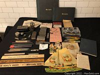 Wide view of various vintage printing items including receipt books, printing blocks, pencils, rulers, metal ink well and pen nibs, wooden rulers with advertising inscriptions, and ephemera arranged on a table.