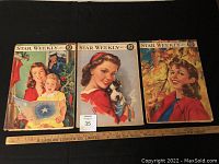 Three Star Weekly magazines displayed side by side on a black surface with a measurement ruler below