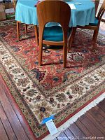Full view of rust-red and cream floral border rug under round table and chairs