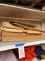 Stack of two wooden folding trays and one metal tray on shelf packed in cardboard box.