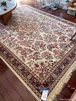 Large area rug laid out on hardwood floor with ivory background and maroon and baby blue floral designs, showing overall pattern and condition