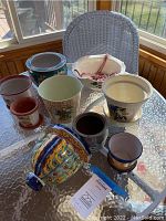 Photo showing a collection of variously sized and colored planters on a glass table with a white wicker chair in background.