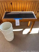 Solid wood indoor plant stand with black grid surface and white porcelain umbrella holder beside it.