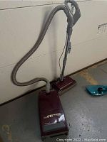 Kenmore Whispertone canister vacuum with hose and upright floor brush attached, shown standing against wall.