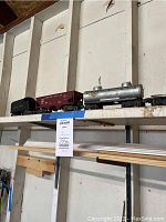Four O scale Lionel train cars displayed on a shelf, including tender, coal hopper, tank car, and flatbed