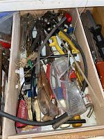 Drawer with assorted hand tools including pliers, screwdrivers, safety goggles, and string.