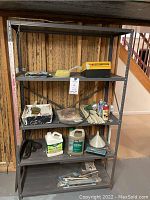 Full view of four tier metal shelving unit with various contents including cleaning supplies, tools, and hardware on shelves.