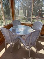 Full view of white wicker patio furniture set with four chairs and round table inside a screened porch.