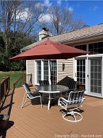 Wide view of deck showing round glass-top table, four chairs, and open red umbrella