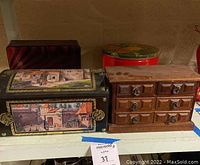 Shelf with German tin storage bin featuring painted village scenes and wooden jewelry box with multiple drawers with metal handles.