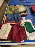 Top view of assorted folded table linens and placemats, including napkins in various colors and a round woven beige placemat.