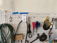 Wide shot of various tools hanging on pegboard including extension cord, pruning shears, saw blade and screwdrivers
