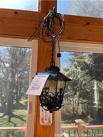 Wide angle shot of black wrought iron hanging lantern suspended from chain with glass panels and ornate scrollwork detailing.
