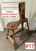 Front-side view of the antique wooden harness makers bench showing shaped seat, upright clamp, and sturdy wooden legs with cross braces and footrests.