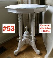 Octagonal side table in white paint shown standing on hardwood floor near couch and window, with turned legs and finial base visible.