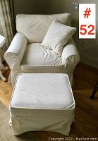 View of arm chair with fitted cream slip cover and matching pillow, accompanied by ottoman with same slip cover on hardwood floor near window.