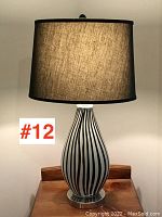 Full view of the lamp lit showing the black and white striped blown glass base with a dark fabric shade.