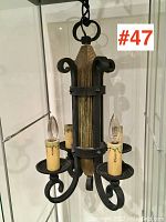 Side angle showing the rustic wood centerpiece and iron scrollwork arms with four candle-style lights.