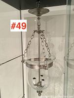 View of entire ceiling light fixture showing metal top, hanging chains, and clear glass shade with three bulb sockets inside.