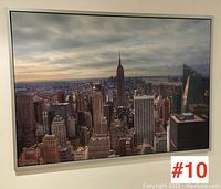 Framed poster print showing the New York City skyline with the Empire State Building prominently in the center, photographed from slightly different angles showing the full frame and print.