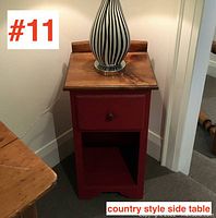 Front view of the pine side table with red milk paint and drawer, lamp on top, showing natural wood grain top and open shelf below.