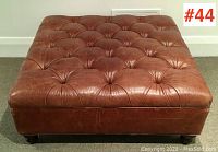 Front-facing view of the square ottoman showing tufted top and wood legs