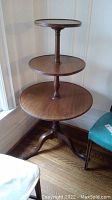 Full view of antique three-tiered wooden table showing all three round shelves and the turned central spindle.