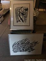 Two hand-painted artworks displayed - one resting on a chair, one leaning against it, showing size and framing