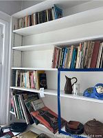 Four shelves of books with some decorative items on the middle shelf, all books arranged standing and some stacked horizontally.