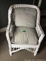 Front view of white wicker chair with beige seat and back cushions, showing woven pattern and armrest design.