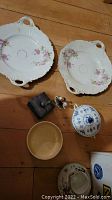 Two white KPM serving plates with pink floral design, small jewelry box, porcelain floral figurine, blue and white covered dish, small brown bowl.