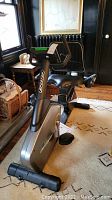 Full side view of the silver and black Sportop magnetic upright exercise bike in a living room setting.