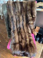 Two brown mink stoles draped lengthwise on chair showing fur exterior.
