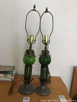 Pair of green glass and metal table lamps 29 inches tall on wooden surface with books in background.